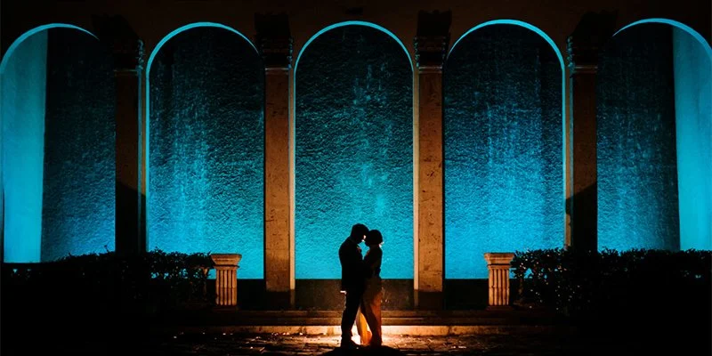 Couple silhouetted in front of the illuminated Waterwall arches at night at The Bell Tower on 34th, Houston, TX.
